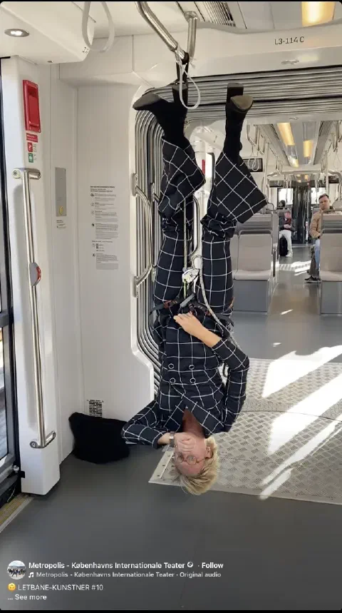 Performer i ternet dragt hænger med hovedet nedad i letbanen
