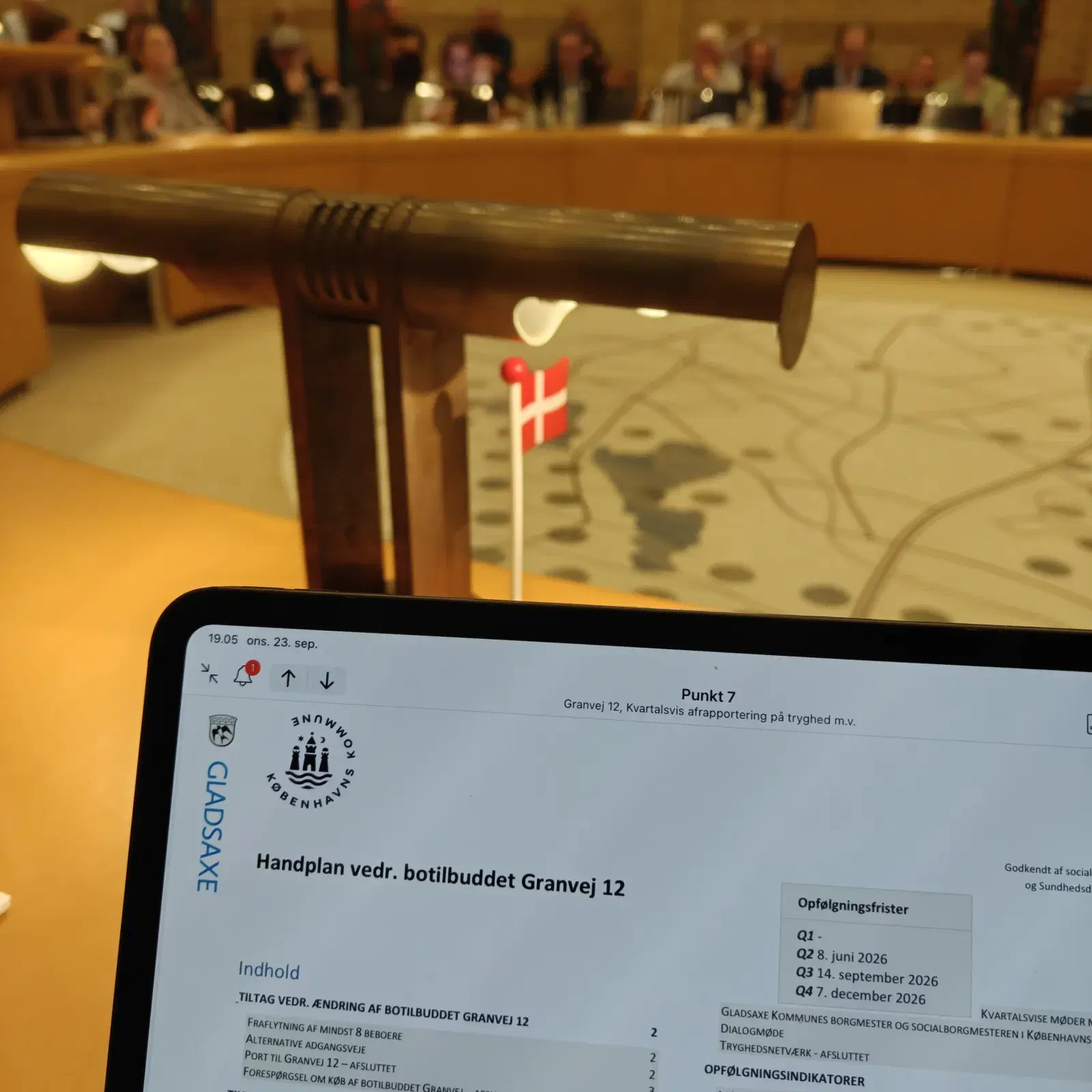 Tablet med kommunens handleplan for botilbuddet Granvej 12 i forgrunden og byrådssalen bagved