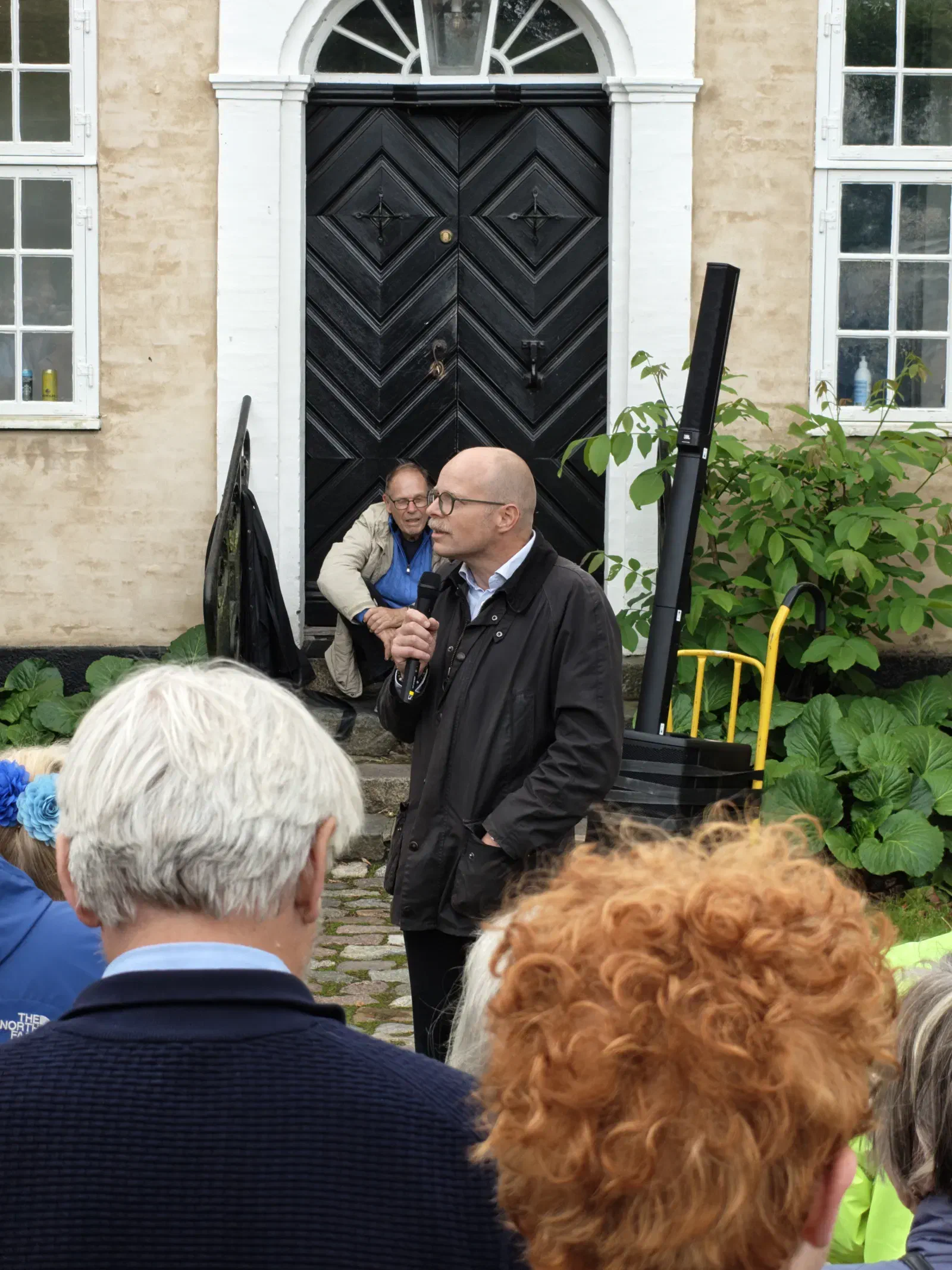 Taler med mikrofon foran Haraldsgaves sorte hoveddør