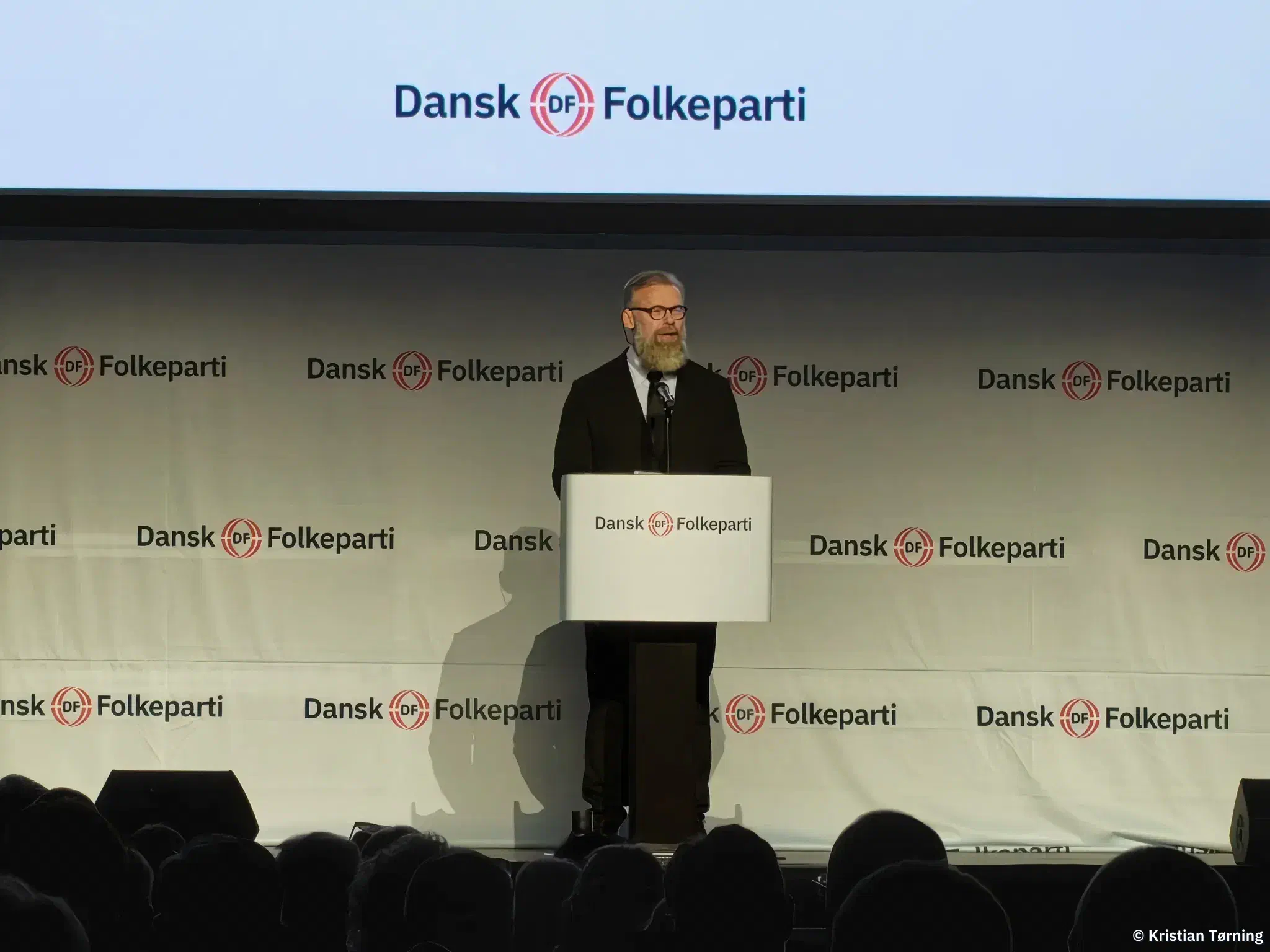 Skægget taler med briller ved talerstolen foran Dansk Folkeparti-logoer