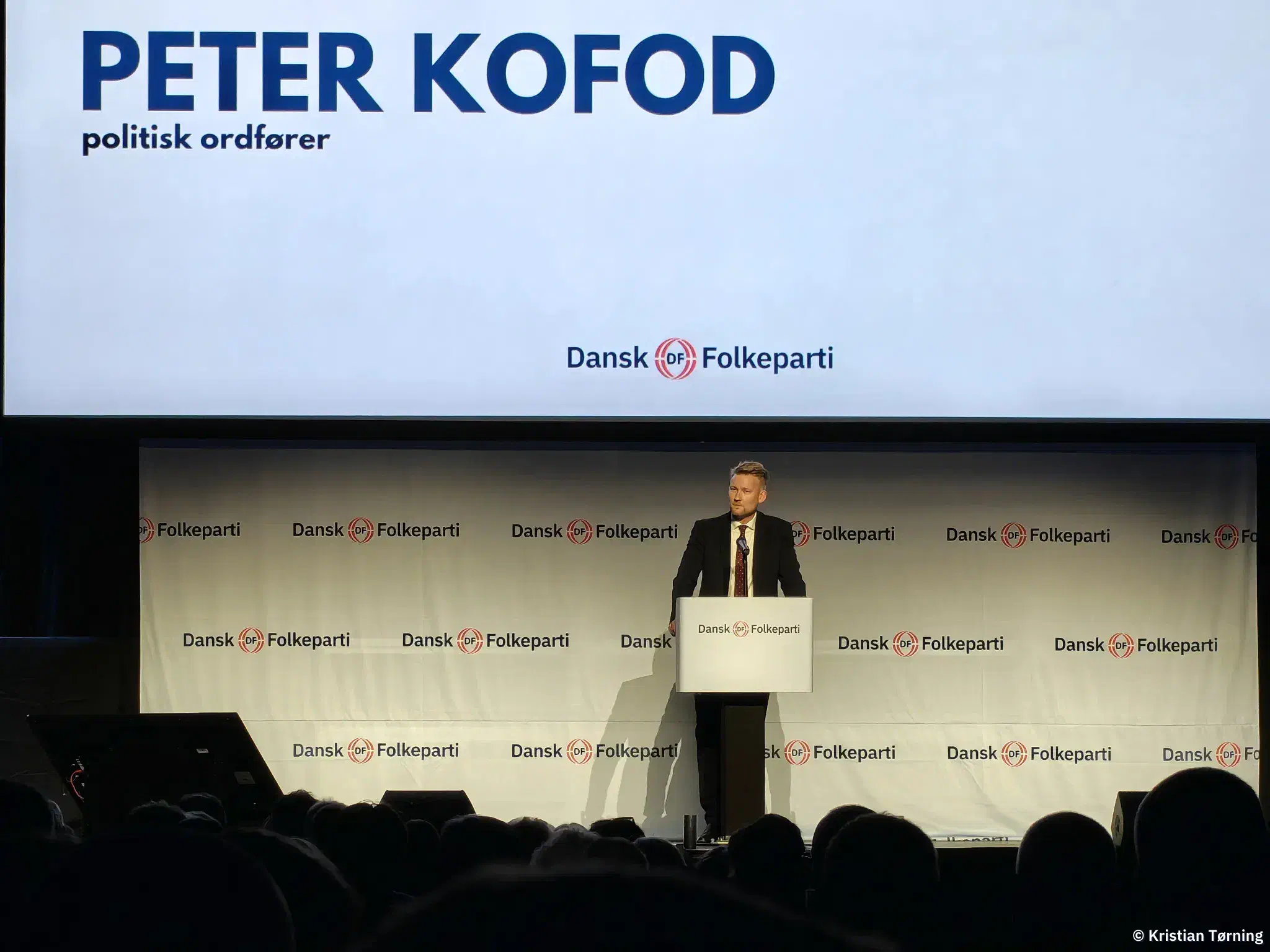 Peter Kofod på talerstolen under en skærm med hans navn