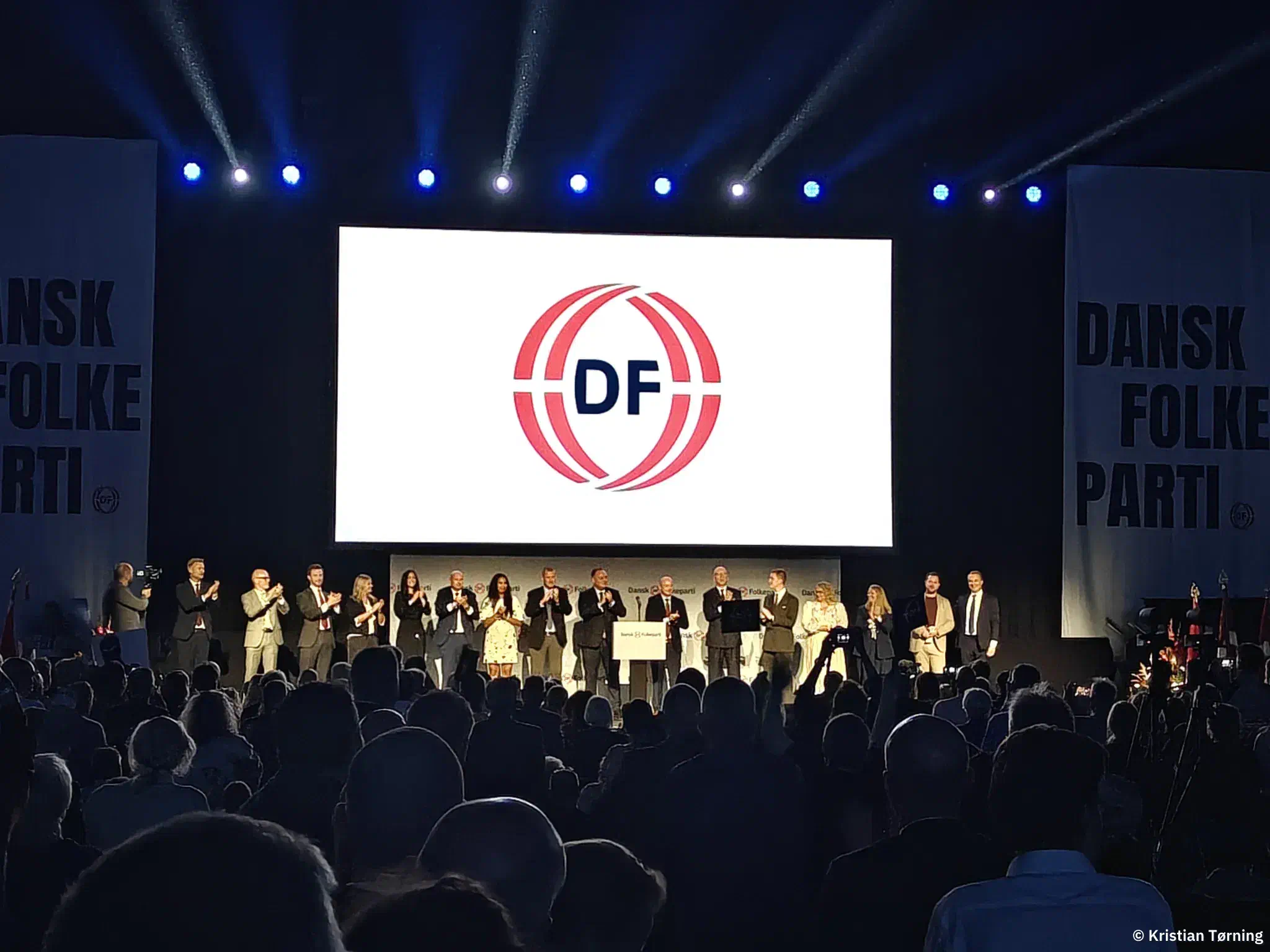 En lang række personer står på scenen under DF-logoet og klapper
