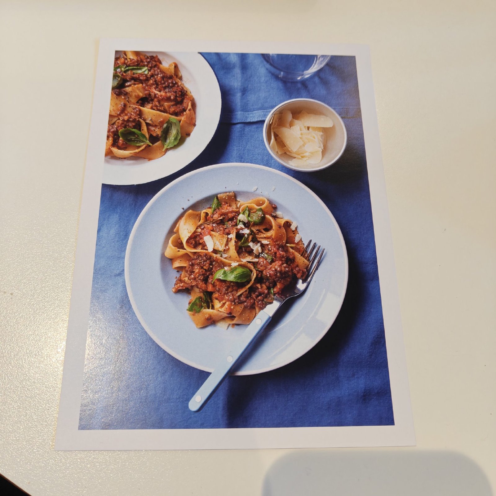 Opskriftskort med foto af pasta med linsebolognese på blå dug